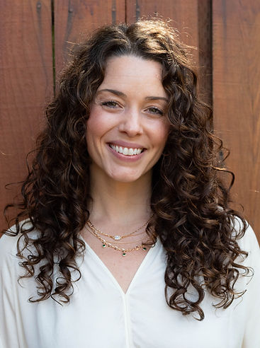 Jacquelyn, founder of The Emerald Soul, smiling in a natural outdoor setting with soft, grounded lighting.