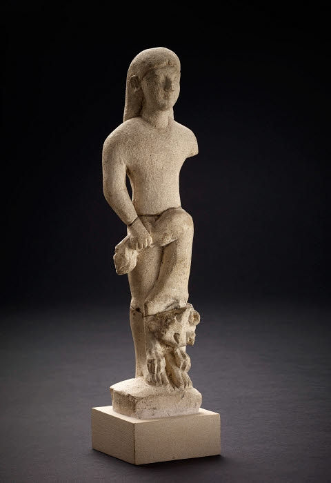 Ancient stone statue of a standing figure with one arm, long hair, and a lion at their feet. Set against a dark background.