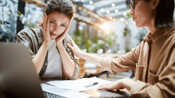 A distressed worker being comforted by another worker as they look at a laptop