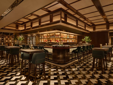 Elegant bar with wood panels, geometric floor, and teal chairs. Shelves display bottles. Warm lighting creates a cosy, sophisticated vibe.