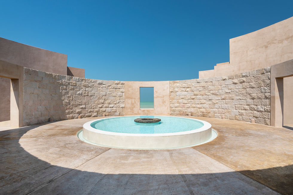 A circular stone courtyard with a small central pool and fountain, surrounded by beige stone walls, under a clear blue sky.