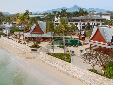 Beachfront resort with Thai-style pavilions, a pool, and palm trees by the shore. Mountains in the background, calm and serene setting.