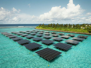Floating solar panels on turquoise water near a green island. Sunny day with white clouds in a blue sky, creating a serene atmosphere.