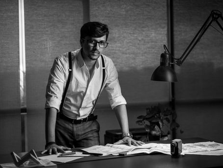 Architect Naveen in a storytelling business portrait, leaning over architectural plans with dramatic studio lighting. Shot by Rakesh Vishwanath