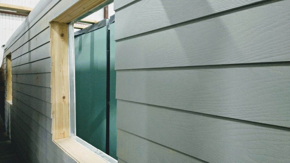 Exterior wall panel with grey horizontal siding and a framed window opening.