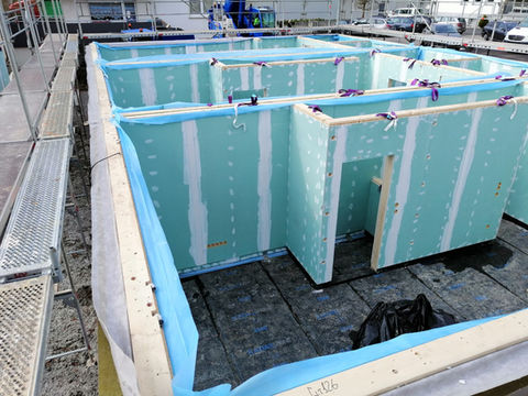 Foundation-level view of a modular house with green prefabricated interior walls assembled on a concrete slab.