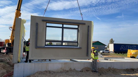 Kran hebt ein vorgefertigtes Wandmodul auf der Baustelle zur Montage.