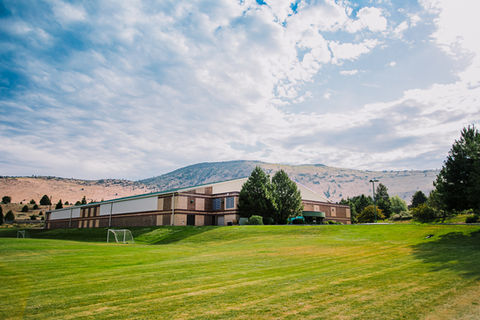 A large building that sits up on a hillside overlooking a soccer field in Klamath Falls.
