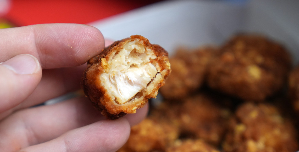 A bite taken out of a chicken nugget, revealing a chunk of white meat.