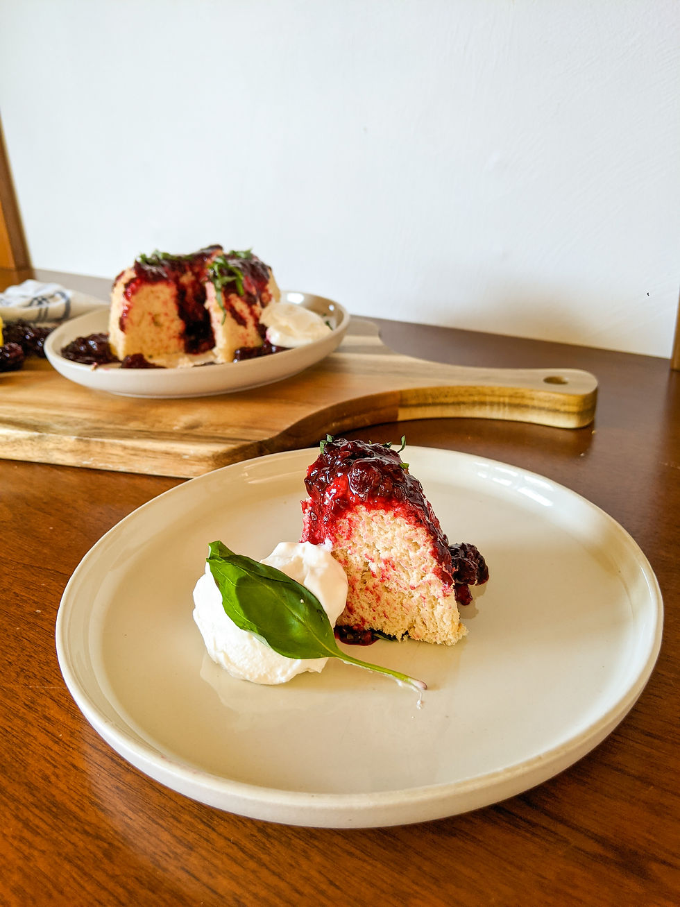 A slice of Paleo Angel Food Cake is shown with a dark, blackberry and Basil Compote drizzled on top