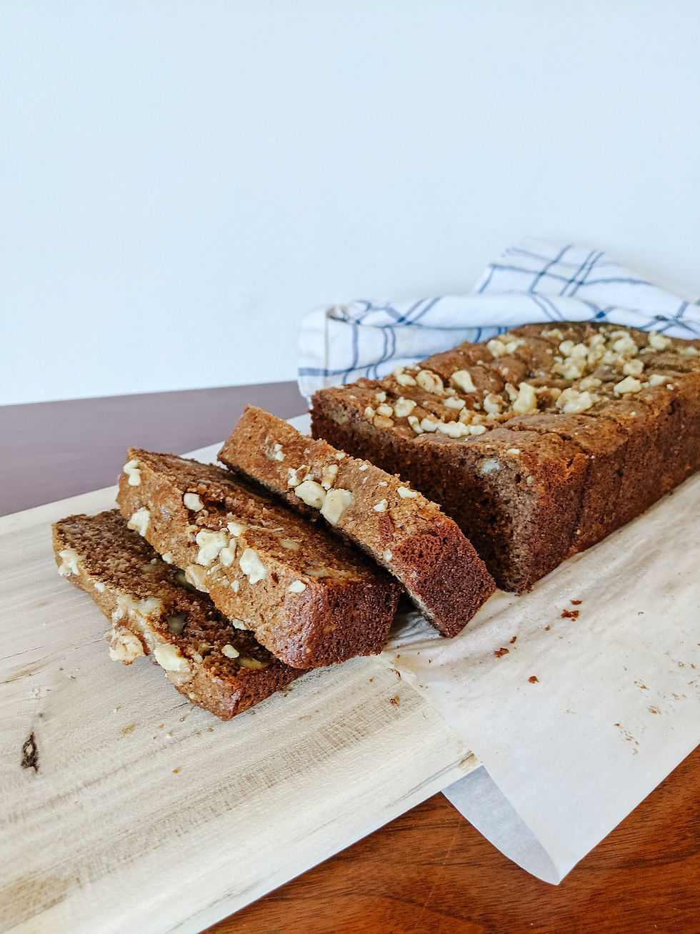 a loaf of paleo banana walnut loaf sits on a wooden block, sliced through out in even slices. The first few slices are tipping over each other. There are walnuts sprinkled on top.