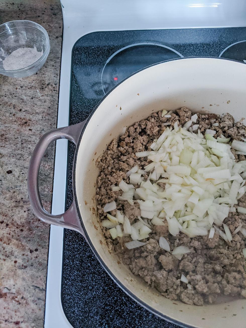 Onions are added to a hot and large Le Crueset Dutch Oven, which already contained cooked ground Italian Sausage.