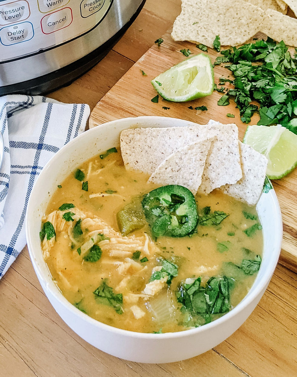 A close up of a cozy bowl of white chicken chili shows fall apart shredded chicken, vibrant cilantro, jalapeno slices, and tortilla chips