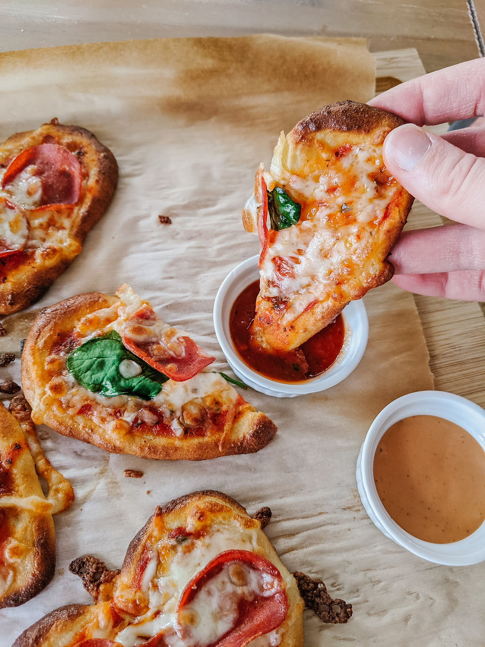 Half of a heart-shaped grain-free pizza is being dipped into a small dish of red marinara sauce.