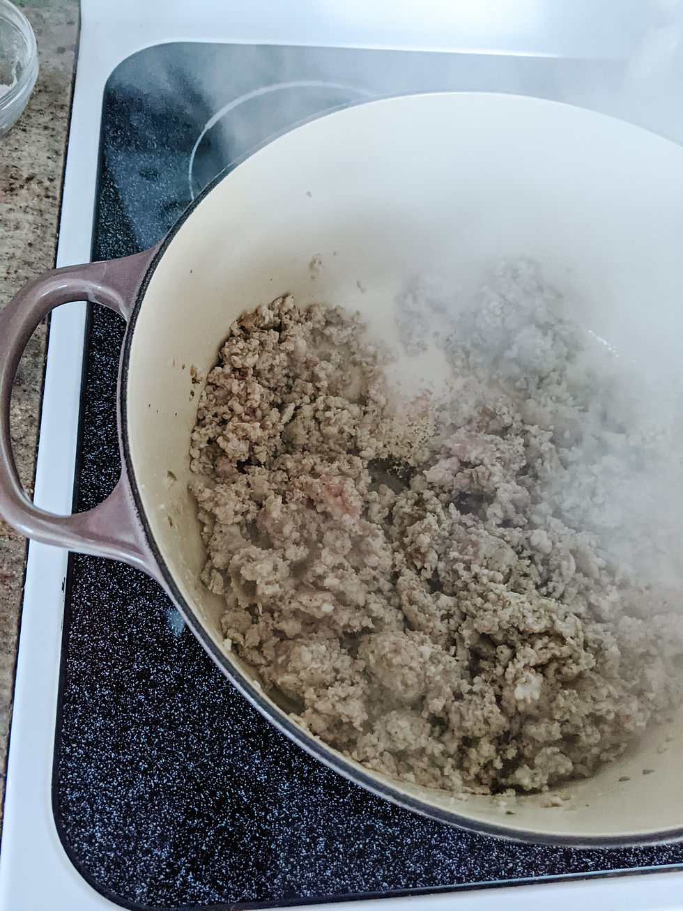 Ground Italian Sausage cooks in a giant Le Crueset dutch oven. The sausage is steaming hot, which is visible in the picture.