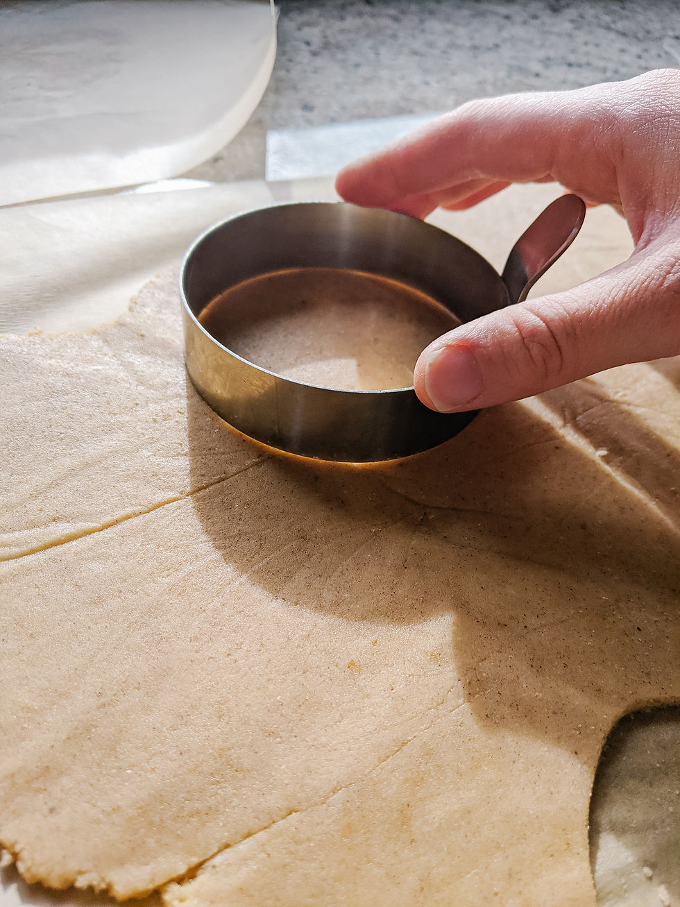 Paleo pastry dough is rolled out flat, while a hand presses a circular cookie cutter into the dough to make miniature tart shells
