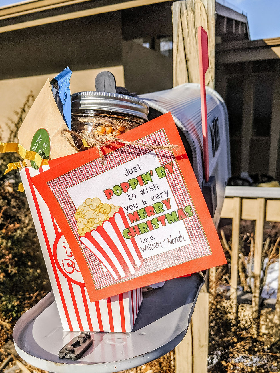 a vintage style popcorn box is filled with a glass mason jar full of popcorn kernels, a brown envelope of popcorn salt, and an individual packet of coconut oil. The empty spaces are filled with crinkled yellow strips of paper, and the box has a cute red and white gift tag that reads, "Just poppin' by to wish you a very Merry Christmas! Love, Norah and William."