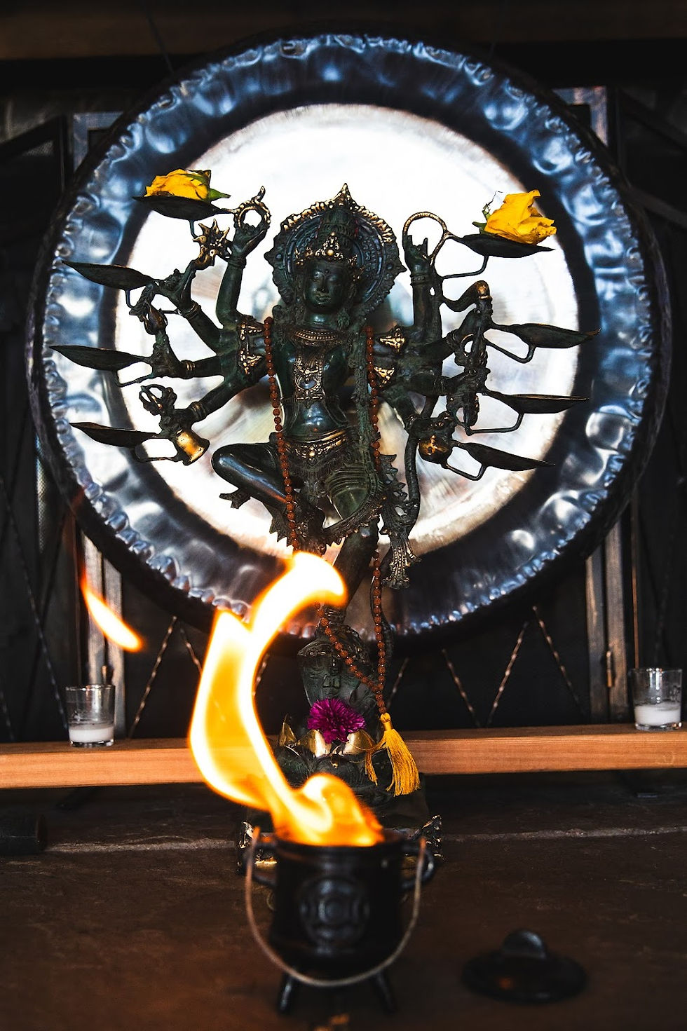 A many-armed bronze deity before a gong, with a flame burning in front of it