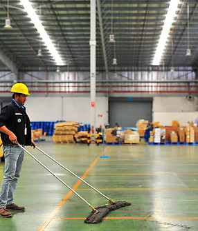 janitor wearing yellow safety helmet and holding a mop cleaning floor warehouse.jpg