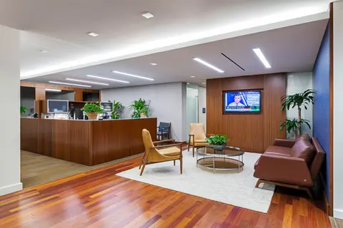Modern office reception area with seating, plants, and television screen. A Pappajohn Company.