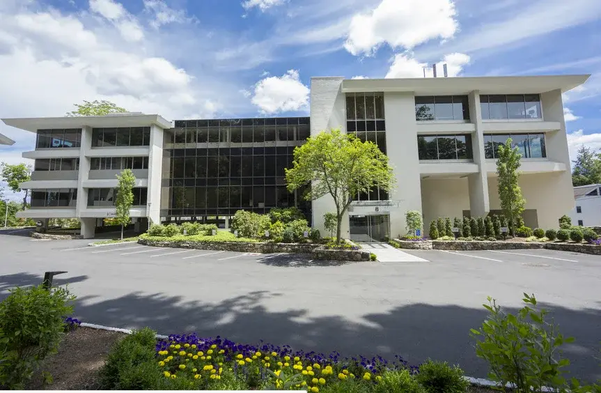 Modern office building with glass windows, bright sky and parking area A Pappajohn Company