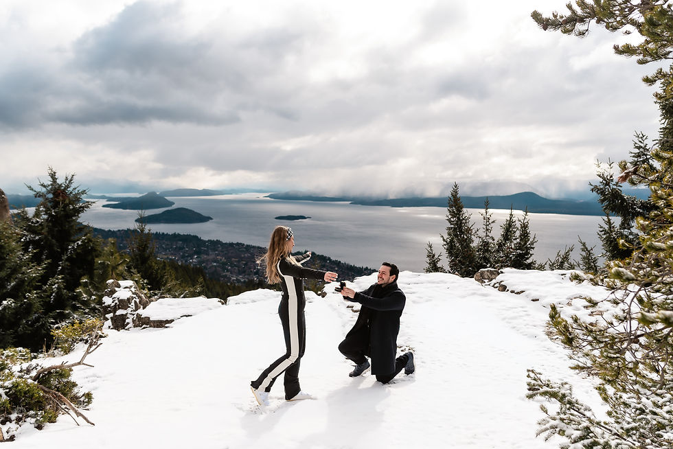 Homem ajoelhado propõe para mulher em cenário nevado, com vista de montanhas e lago ao fundo. Céu nublado, atmosfera romântica. Ensaio na Neve em Bariloche - Davi Minatto Fotógrafo Brasileiro em Bariloche