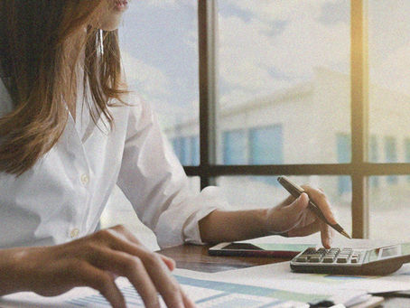 A woman doing calculations with self storage units visible outside the window behind her