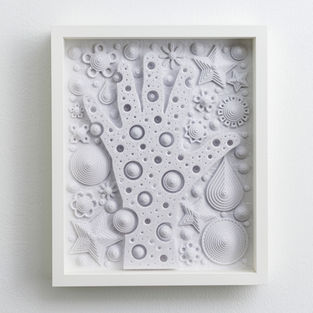 white paper sculpture of hand circles and stars in a white frame hanging on a wall