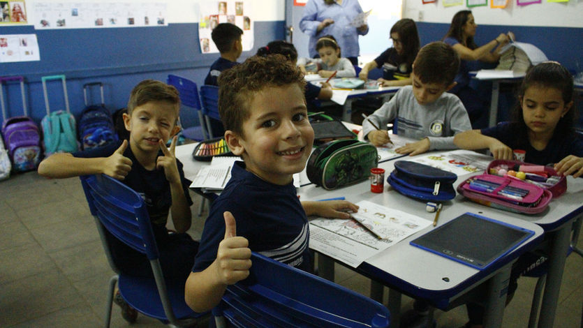Crianças felizes em sala de aula, mostrando o polegar para cima