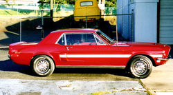 Side view of 1968 Ford Mustang painted red with white stripe down side.