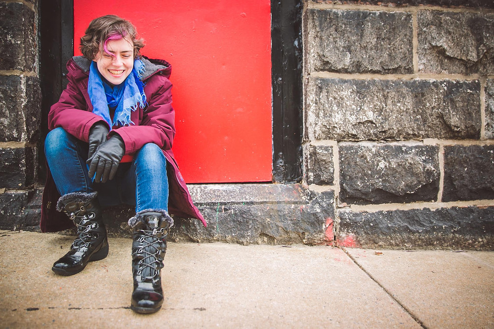 Sarah Blake by JPG Photography. Author of Mr. West, Let's Not Live on Earth and Naamah. Brick wall, red door, jeans, gloves and boots.