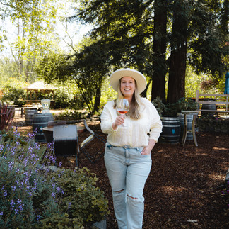Girl holding glass of wine surrounded by redwood trees and purple flowers 