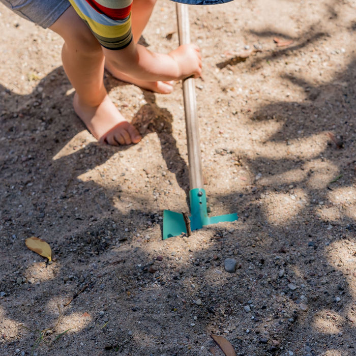 Kind spielt im Sand mit einem grünen Rechen. Ferienbauernhof Mau
