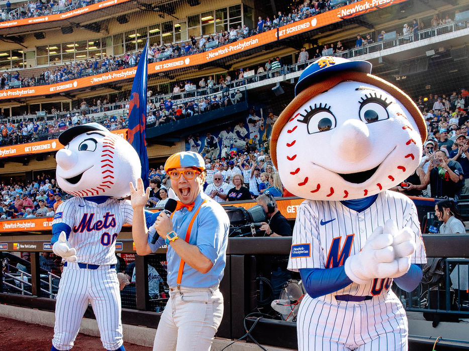 Blippi with Mets mascots holding mics at a baseball game.