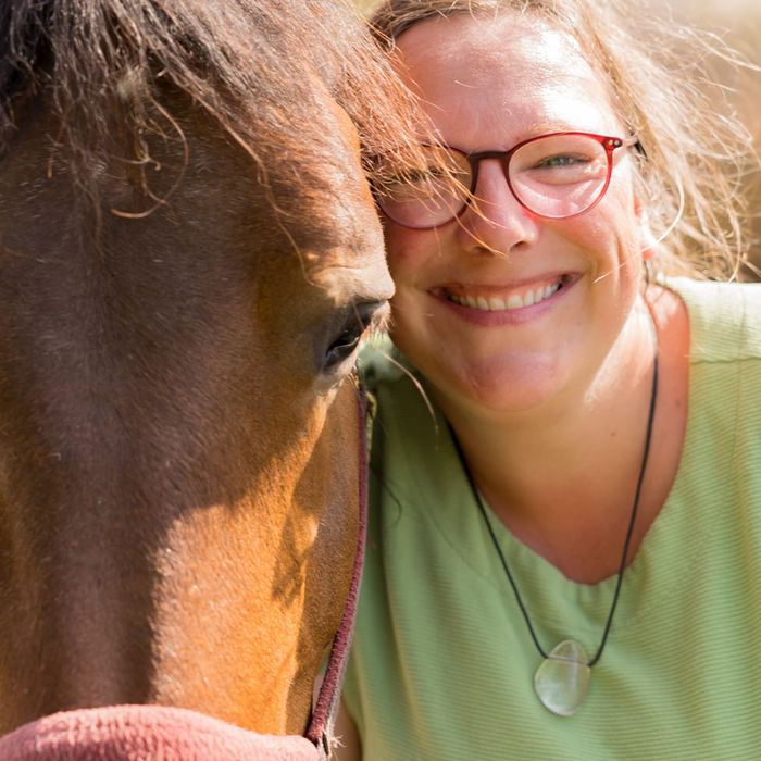 Woman smiles with horse, wearing glasses and green shirt; close up.