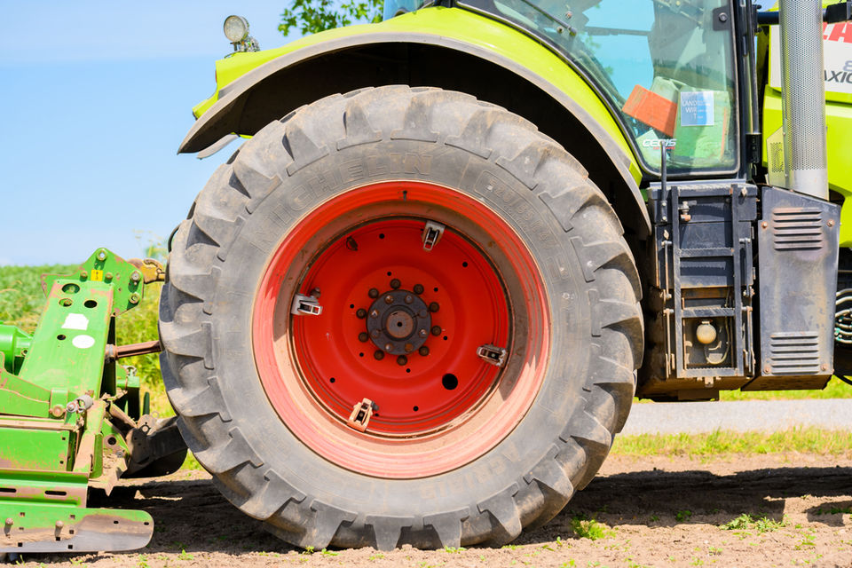Nahaufnahme des Reifens eines grünen Traktors, roter Felge und Feldhintergrund.