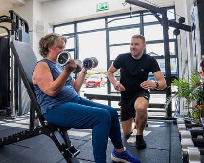 Woman lifting weights with trainer in gym setting, photography and videography.