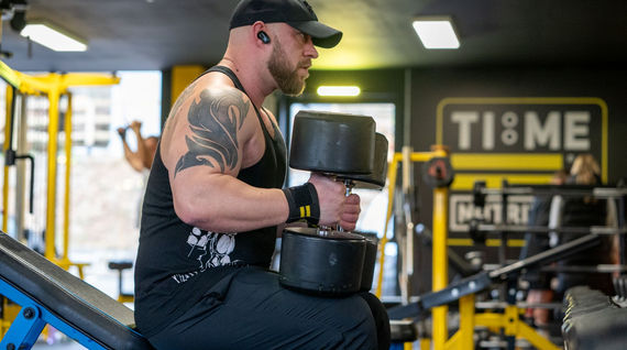 Weightlifter using dumbbells at gym with logo in background, fitness photography.
