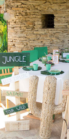 Dschungel Backdrop mit einem Tisch der dekoriert für Dschungel ist, eine Willkommenstafel und einen Kaktus.