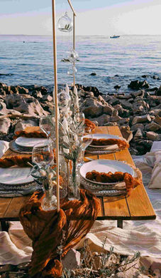 Picknicktisch in Rostrot mit goldenen Kerzenständern am Meer.