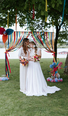 Brautpaar vor einem rechteckigen Traubogen mit vielen verschiedenfärbigen Bändern als Dekoration.