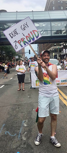 man marching in pride parade with "Deaf, Gay, and Proud" sign