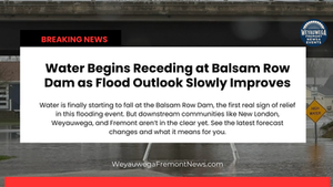 Breaking News: Water recedes at Balsam Row Dam; flood outlook improves. High water sign visible. Houses in background.