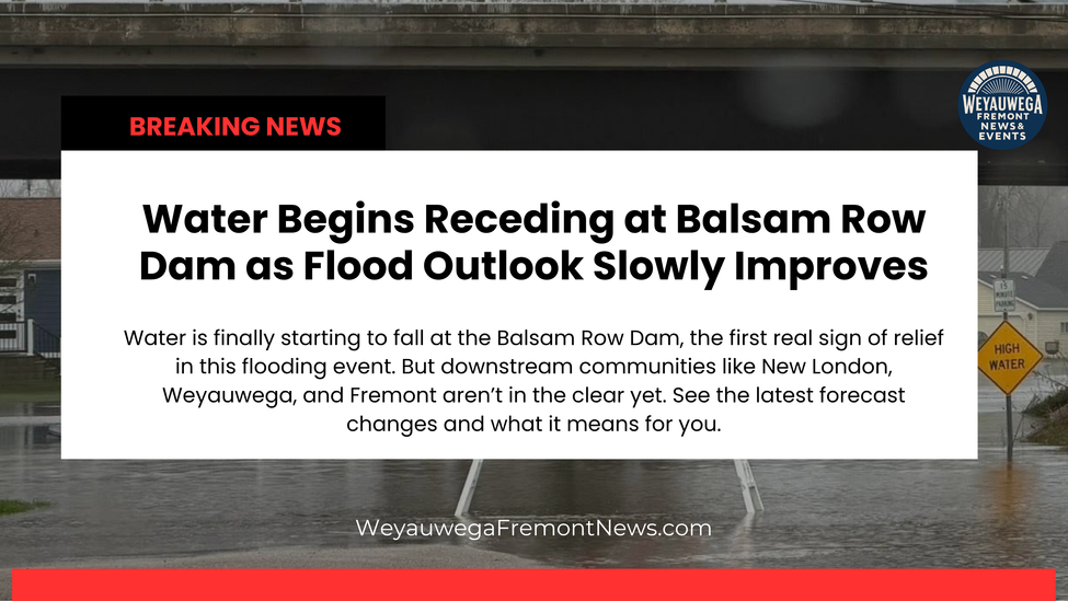 Breaking News: Water recedes at Balsam Row Dam; flood outlook improves. High water sign visible. Houses in background.