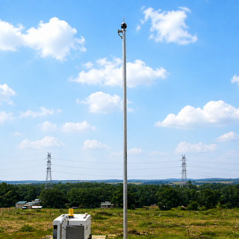 Tall monitoring pole in a field with power lines behind.