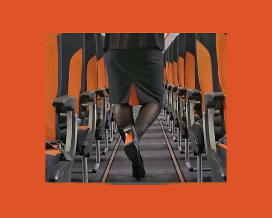 Hôtesse de l’air en uniforme marchant dans la cabine d’un avion, sièges orange, tenue professionnelle aérienne. 