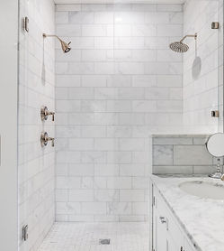 Elegant custom tile shower with marble walls, glass enclosure, and dual showerheads, designed by Chattanooga Tile Company in Chattanooga, Tennessee.