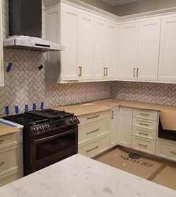 Kitchen backsplash installation with herringbone tile pattern, complementing white cabinets and marble countertops by Chattanooga Tile Company in Chattanooga, Tennessee.