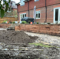 Empty patio space with new fencing and unfinished paving, landscaping in progress.