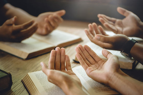 Christian group of people holding hands praying worship to believe and Bible on a wooden t
